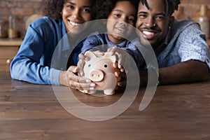 Happy African couple and little daughter posing indoor with piggybank