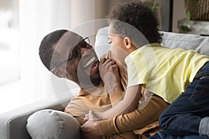 Happy african dad laughing playing with little toddler son together