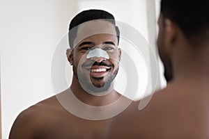 Happy african ethnicity man cleansing pores with removal strip.