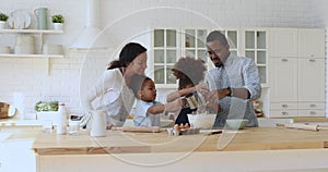 Happy african ethnicity parents watching kids siblings cooking.