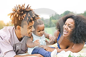 Happy African family enjoying a picnic sunny day outdoor - Mother and father having fun with their daughter in a public park