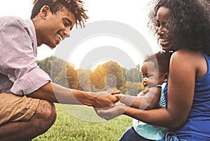 Happy African family enjoying time together in public park - Mother and father having fun playing with their daughter at sunset