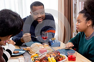 Happy African family father feeding food with daughter in dinner on festive thanksgiving eve day together at home.