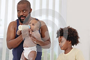 Happy African family, father feeds toddle baby infant after take a bath and apply talcum powder on body in bathroom. Little photo