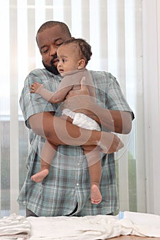 Happy African family, father holding his toddle baby infant daughter after ready taking a bath applying talcum powder on body in photo