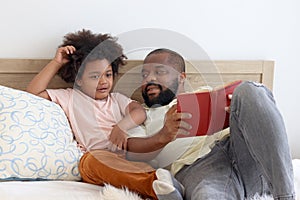 Happy African family, father and son spending time together, young boy with black curly hair and dad reading a book together while