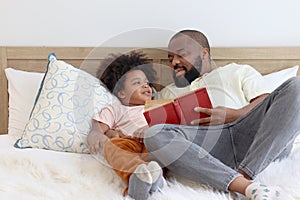 Happy African family, father and son spending time together, young boy with black curly hair and dad reading a book together while