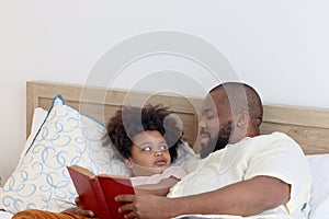 Happy African family, father and son spending time together, young boy with black curly hair and dad reading a book together while