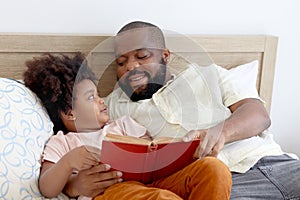 Happy African family, father and son spending time together, young boy with black curly hair and dad reading a book together while