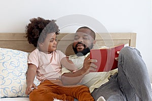 Happy African family, father and son spending time together, young boy with black curly hair and dad reading a book together while