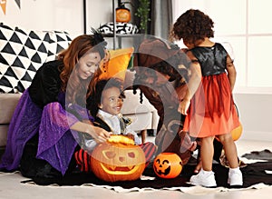 Happy african family in Halloween costumes sitting on floor with carved pumpkin jack-o-lantern