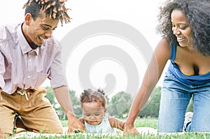 Happy African family having fun doing picnic in public park - Mother and father playing with their daughter outdoor