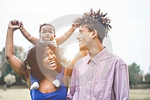 Happy african family having fun outdoor during sunny day in public park - Dad, mum and daughter enjoying tender moments together