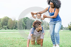 Happy african family having fun in a public park outdoor - Mother and father playing with their daughter during a weekend