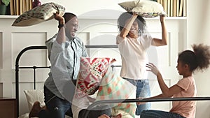 Happy african family and kids having pillow fight on bed