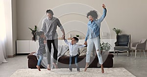 Happy African family with kids holding hands jumping indoors