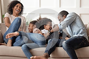 Happy african family with kids tickle laugh sit on sofa