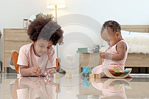 Happy African family spending time together, brother boy with black curly hair lying on floor, playing toy with little cute toddle