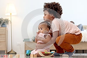 Happy African family spending time together, brother boy with black curly hair try to hold and lift up little cute toddle baby