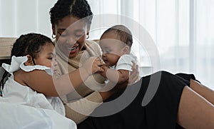Happy African family, young mother and daughters, little kid older sister looking and tender holding her newborn sister hand