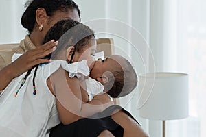 Happy African family, young mother and daughters, little kid older sister tender kissing her newborn baby sister hand