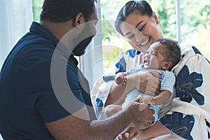 Happy African father and Asian beautiful mother holding carrying cute newborn baby in arms, playing and looking at infant with
