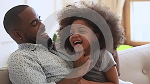 Happy african father and child daughter tickling sit on sofa