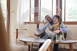 Happy African Father and little child son spending time playing wooden airplane toy at home together