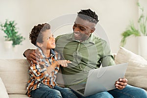 Happy african father and son sitting with laptop at home