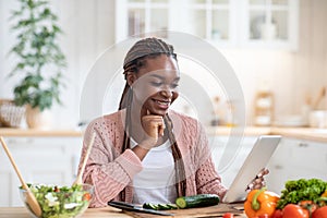Happy african female checking recipe on digital tablet while cooking in kitchen