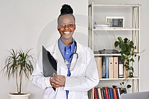 Happy african female doctor looking at camera standing holding clipboard.