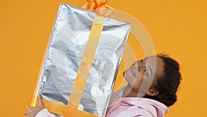 Happy african female holding sizable gift box in hands, holiday package, sale