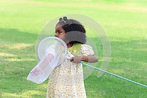 Happy African girl with black curly hair holds scoop-net for catching insect bug and butterfly in green garden. Child explores