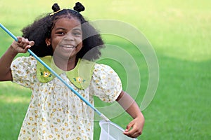 Happy African girl with black curly hair holds scoop-net for catching insect bug and butterfly in green garden. Child explores