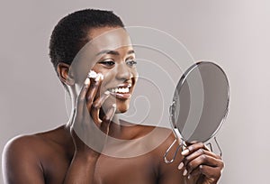 Happy African Girl Looking in Mirror And Applying Face Cream