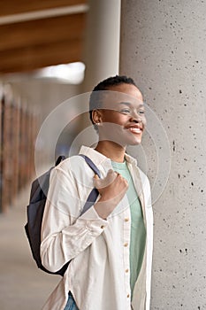 Happy African girl student holding backpack standing in library, vertical.