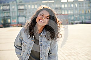 Happy African girl wearing denim jacket looking at camera standing on street.