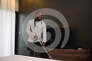 Happy African guy cleaning floor with a mop in bedroom. Household and cleaning concept