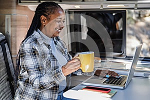 Happy african having fun woman using computer laptop inside mini camper van - Focus on face