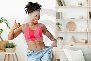 African Lady Gesturing Thumbs-Up Wearing Oversize Jeans After Slimming Indoor photo