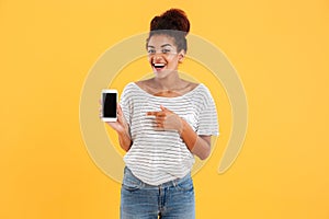 Happy african lady showing smartphone with blank screen isolated