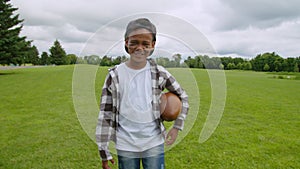 Happy african little boy with american football ball walking on pitch