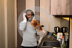 Happy African man listening to music in headphones and singing while doing housework