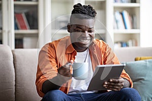 Happy african man using digital tablet, drinking coffee