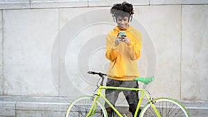 Happy African man using mobile smartphone outdoor while riding with bike in the city