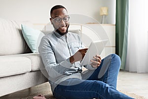 Happy African Man Using Tablet Browsing Internet Sitting At Home
