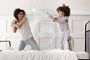 Happy african mom and daughter having pillow fight on bed