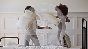 Happy african mom and daughter playing pillow fight on bed