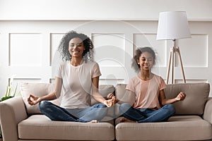 Happy african mom teaching kid daughter doing yoga at home