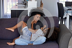 Happy african mom tickling kid daughter laughing together on couch